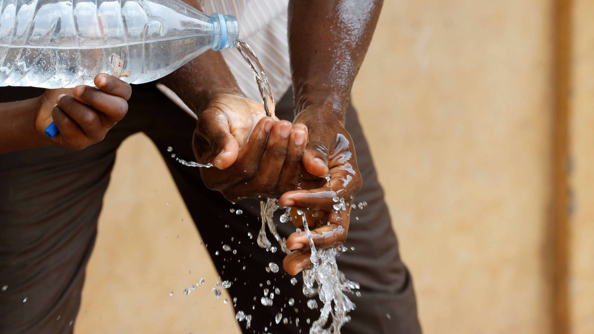 Water being poured out of a bottle to wash hands, symbolizing scarcity of drinking water