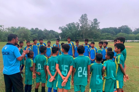 Two boys' soccer teams stand in a circle and receive a speech from the coach