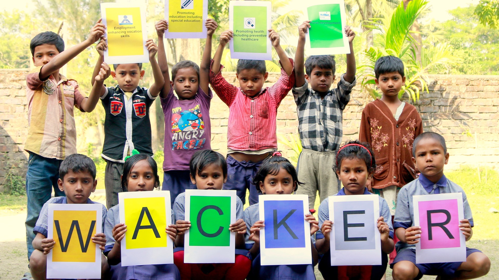 A group of 12 children hold up colorful signs displaying the CSR goals and the word WACKER.