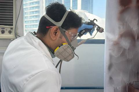 A laboratory employee from Dubai wearing a protective mask sprays a wall for test purposes