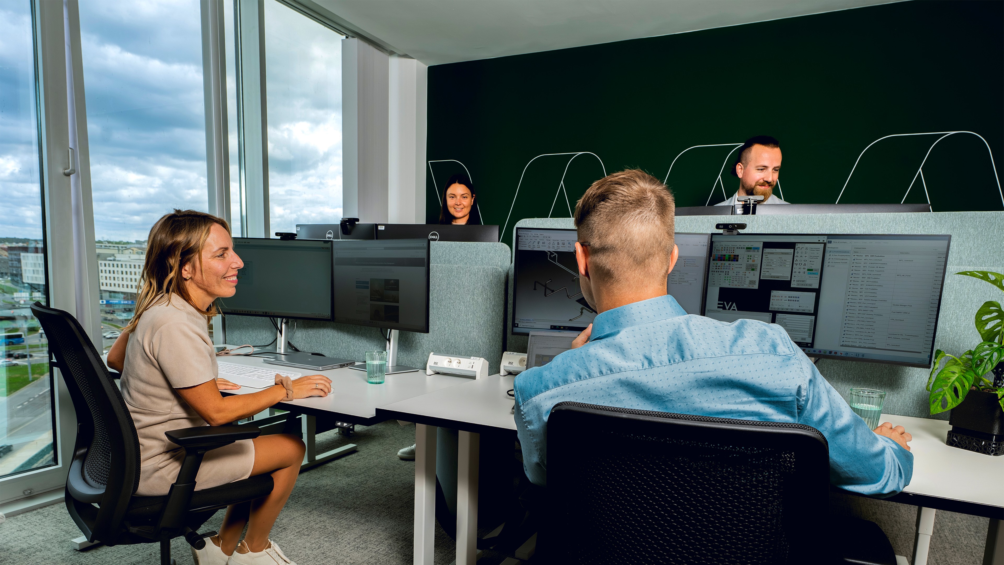 Vier Personen sitzen mit fr&ouml;hlichen Gesichtern in einem B&uuml;ro an ihren Schreibtischen.