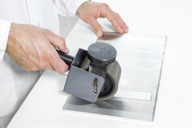 A lab technician using a roller to apply a defined amount of pressure to various test strips in order to determine their release properties. 