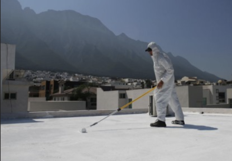 A worker in protective clothing uses a roller to apply a liquid waterproofing system modified with hybrid polymers to a flat roof. 