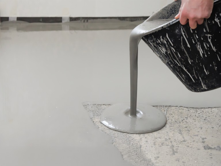 Pouring self-leveling compound onto a prepared floor surface for even and smooth subfloor leveling.