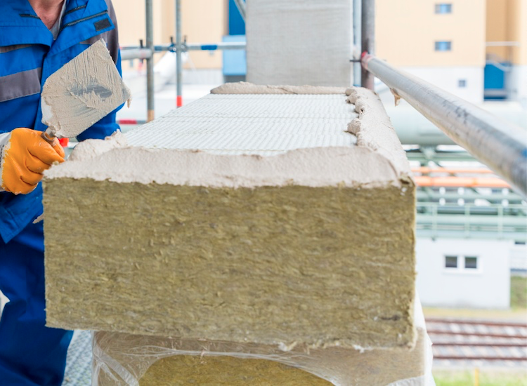 Application of adhesive mortar modified with polymer binder to a mineral wool insulation panel during facade insulation installation.